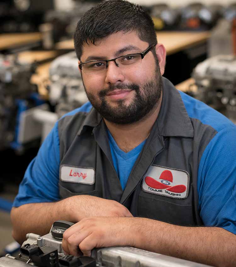 ford asset student smiling at camera while working on the gas cap area of a car
