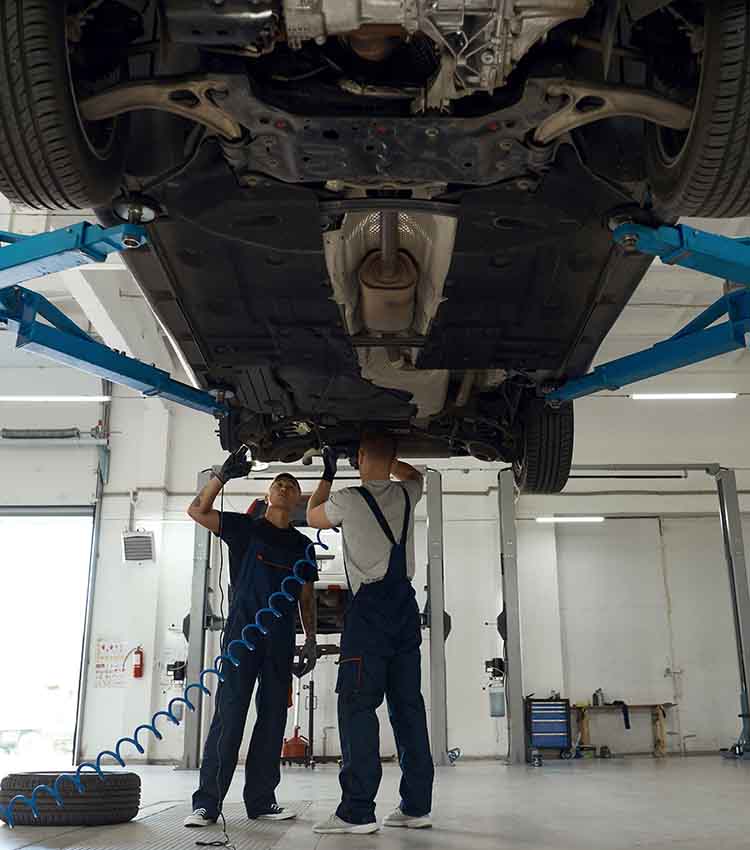 two general motors mechanics working on the undercarriage of a car